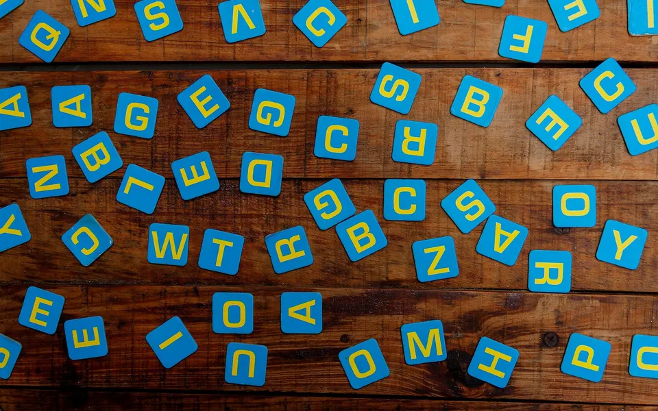 Peças azuis com letras amarelas espalhadas sobre uma mesa de madeira.